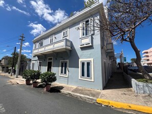 A two-story building with a balcony, a gated entrance, and a small tree in the foreground. - Cozy 1BR Apartment in San Juan with Full AC - 2 (San Juan)
