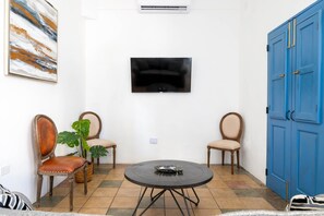 A room with a TV mounted on the wall, two chairs, a round table, and a blue cabinet. - Cozy 1BR Apartment in San Juan with Full AC - 2 (San Juan)