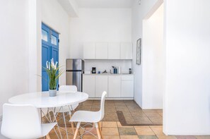 A compact kitchen with white cabinets, a blue door, and a dining area with a white table and chairs. - Cozy 1BR Apartment in San Juan with Full AC - 2 (San Juan)