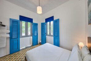 A room with a bed, two windows with blue shutters, a hanging light fixture, and a tiled floor. - Charming San Juan Getaway | AC & Fast Wi-Fi - 3 (San Juan)