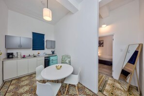 Une cuisine compacte dotée d’appareils électroménagers modernes, un coin repas avec une table ronde et des chaises, et une chambre à coucher avec un lit et un grand miroir.