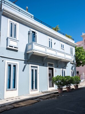 A two-story building with a balcony, potted plants, and a clear blue sky.