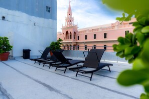 A rooftop terrace with four lounge chairs, a potted plant, and a trash bin.