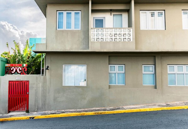 A multi-story building with a flat facade, multiple windows, and a red gate.