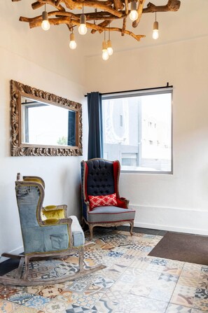 A room with a large mirror, a window with curtains, a patterned rug, and two chairs with unique designs.