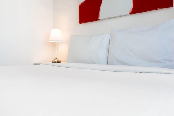 A hotel room with a bed, a nightstand, and a lamp.