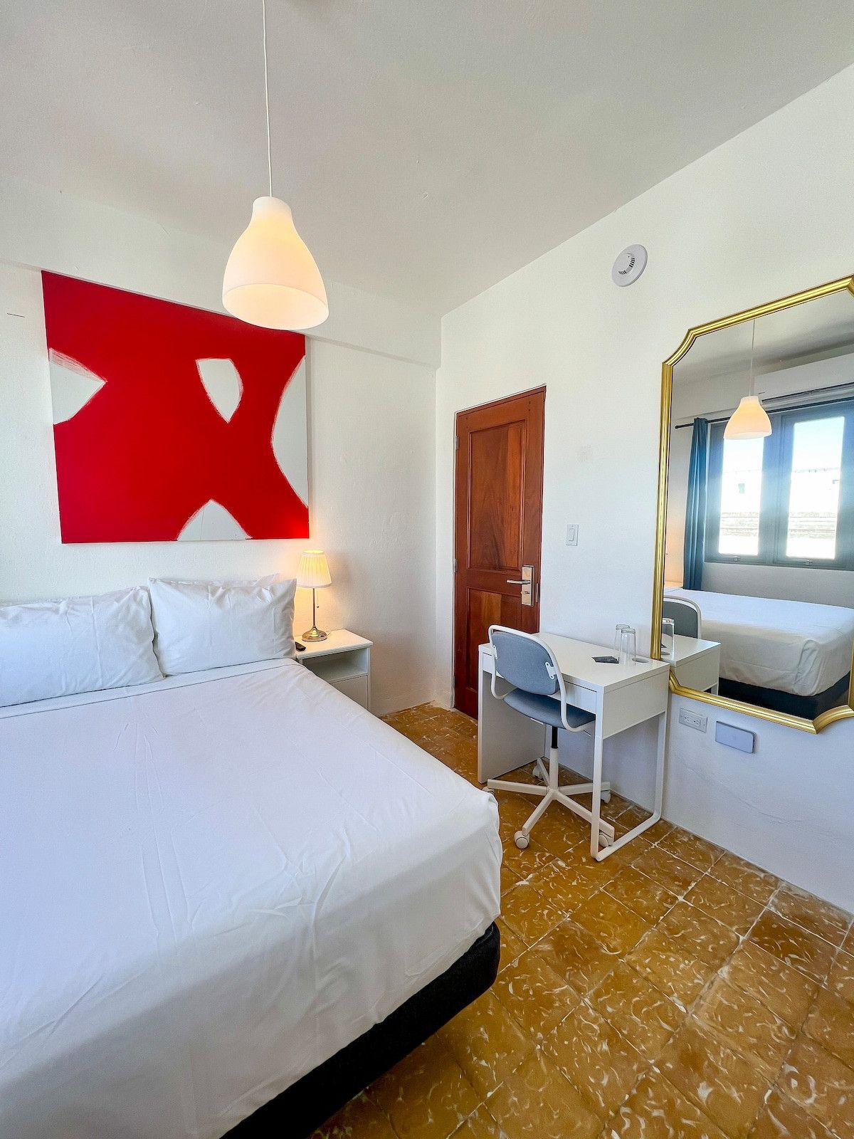 A hotel room with a bed, desk, chair, and a large mirror.