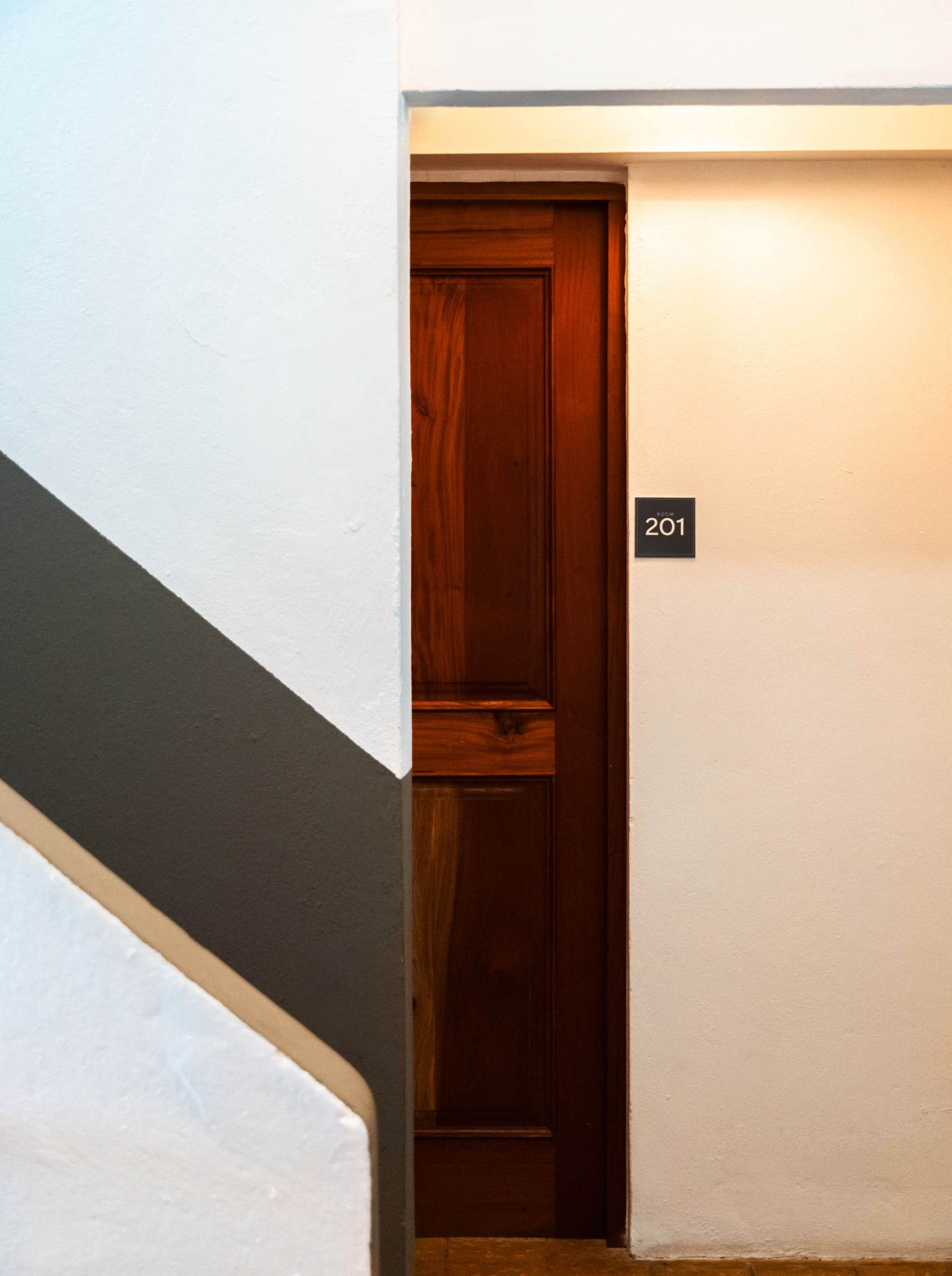 A wooden door with a room number sign, a white wall, and a dark floor.