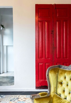 Une pièce avec une porte rouge, un fauteuil jaune et un sol à motifs.
