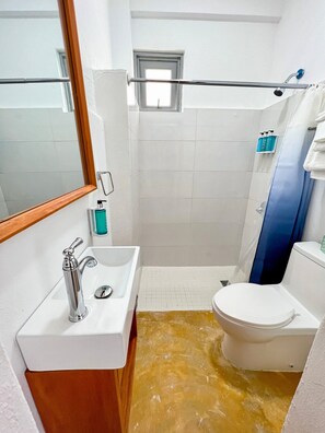 Een badkamer met een wit wastafelmeubel, een toilet en een douche.