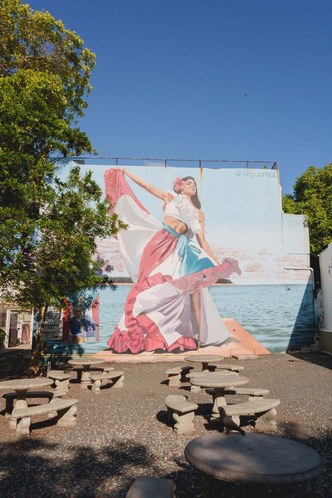A mural of a woman in a flowing dress with a bird perched on a stone bench.