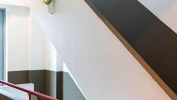 Una escalera moderna con barandilla roja y una planta en maceta en la pared.