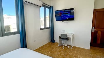 A hotel room with a bed, a desk, a television, and a window with curtains.