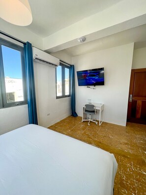 Une chambre d’hôtel avec un lit, un bureau, une télévision et une fenêtre avec des rideaux.