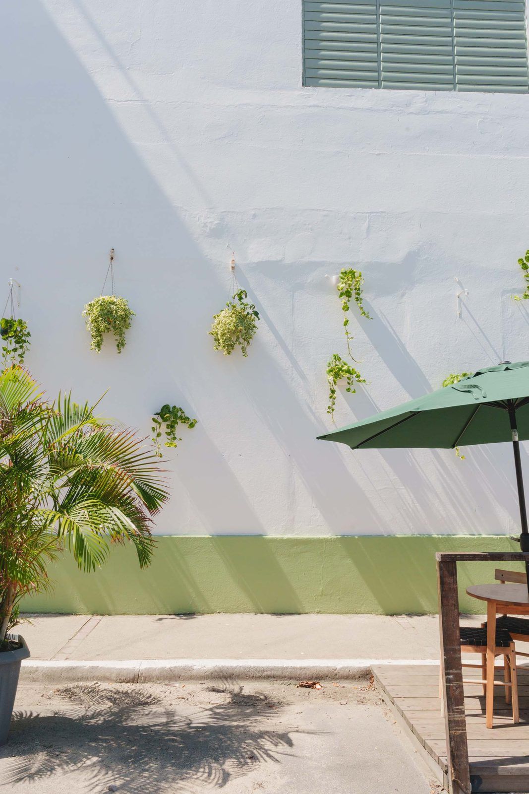 Un espace patio avec un mur blanc, une partie inférieure verte et des plantes suspendues.