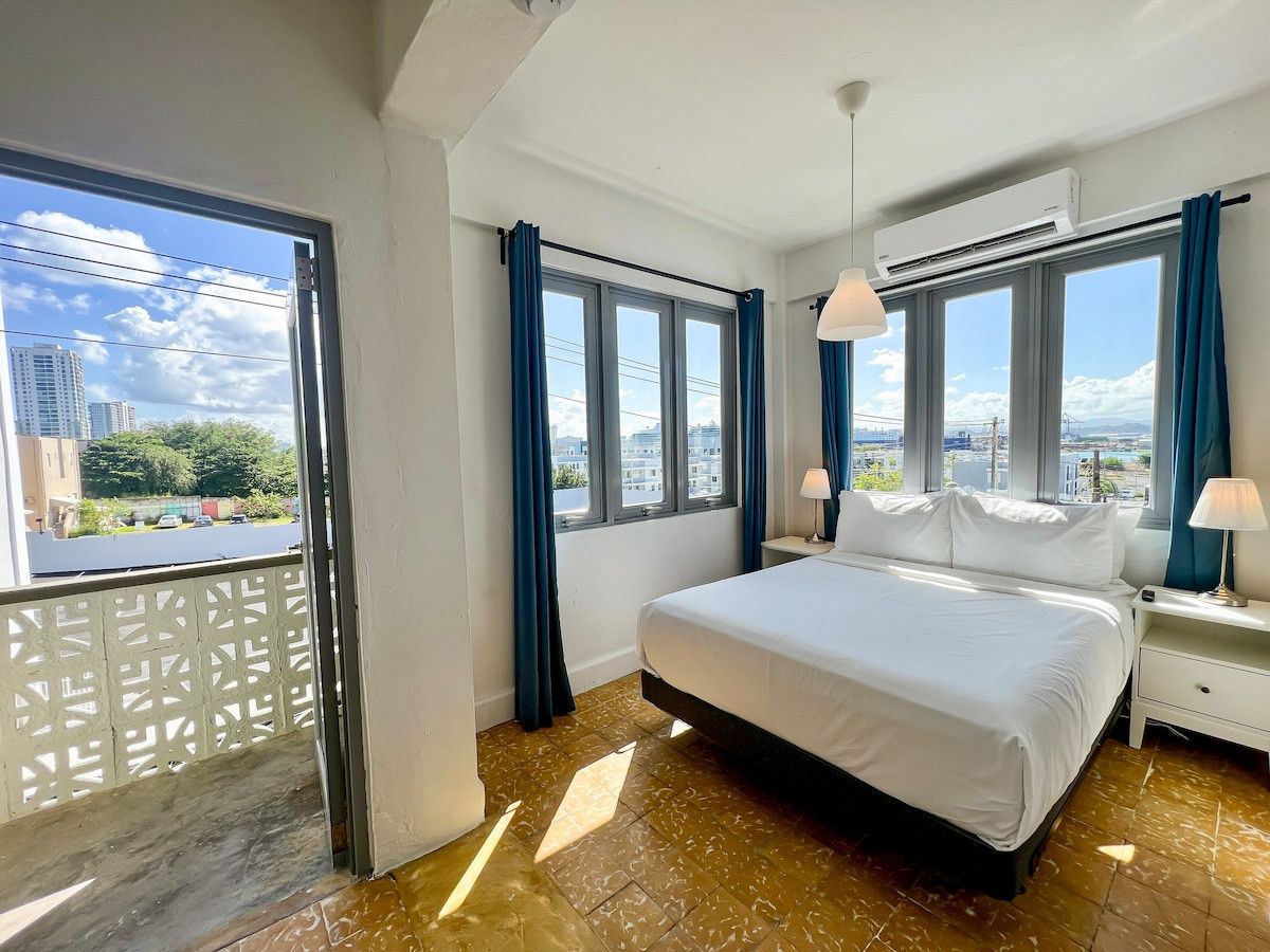 Une chambre d’hôtel avec un grand lit, deux tables de chevet, une fenêtre avec des rideaux et un appareil de climatisation.