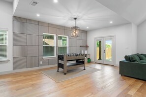 A modern living room with a wooden floor, a green sofa, a foosball table, and a patterned wall. - Spacious Dallas Retreat - Sleeps 10 - Near Downtown & Trinity Groves (Dallas)