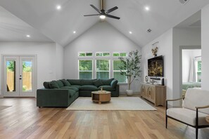Ein modernes Wohnzimmer mit einem Ecksofa, einem Deckenventilator und einem großen Fenster mit Jalousien.