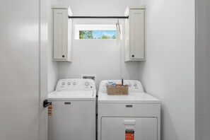 A laundry room with two Maytag washers and dryers, a small window with a view of trees, and a hanging rack above the dryers. - Spacious Dallas Retreat - Sleeps 10 - Near Downtown & Trinity Groves (Dallas)