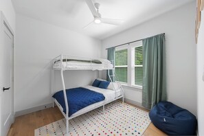 Ein Schlafzimmer mit Etagenbetten, einem Deckenventilator, einem Fenster mit grünen Vorhängen und einem Teppich mit Punkten.