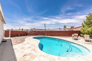 Uma piscina com design curvo, rodeada por um pátio pavimentado e uma cerca de madeira.