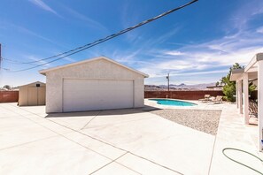 A residential backyard with a garage, a swimming pool, and a clear view of mountains in the distance. - Spacious POOL Home-3 Bedrooms & 3 Full Baths, With An Abundant Parking Area (Lake Havasu City)