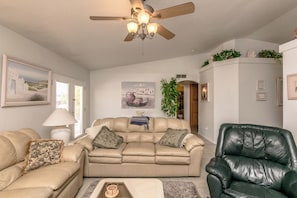 Ein Wohnzimmer mit einem beigen Sofa, einem grünen Ledersessel, einem Deckenventilator und Wandbildern.