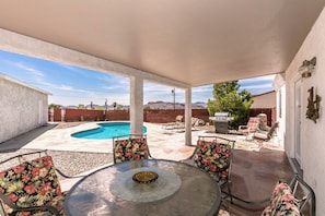 Eine überdachte Terrasse mit Pool, Gartenmöbeln und Blick auf Berge.