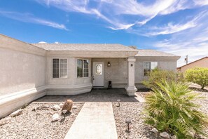 A single-story house with a front porch, a small entryway, and a garden with rocks and plants. - Spacious POOL Home-3 Bedrooms & 3 Full Baths, With An Abundant Parking Area (Lake Havasu City)
