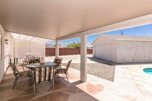 Uma área de varanda coberta com mesa redonda e cadeiras, piscina e garagem.