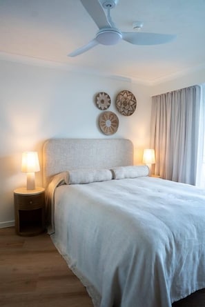 A bedroom with a bed, nightstands, wall decor, a ceiling fan, and a window with curtains. - Everlong- Palm Beach (Gold Coast)