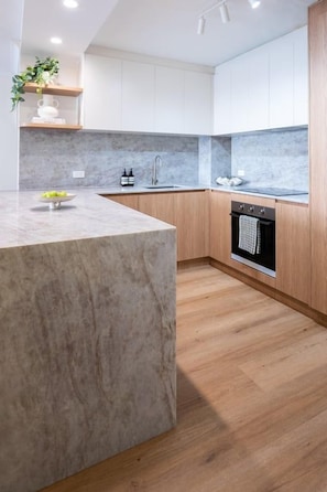 A modern kitchen with a marble countertop, wooden cabinets, and a built-in oven. - Everlong- Palm Beach (Gold Coast)