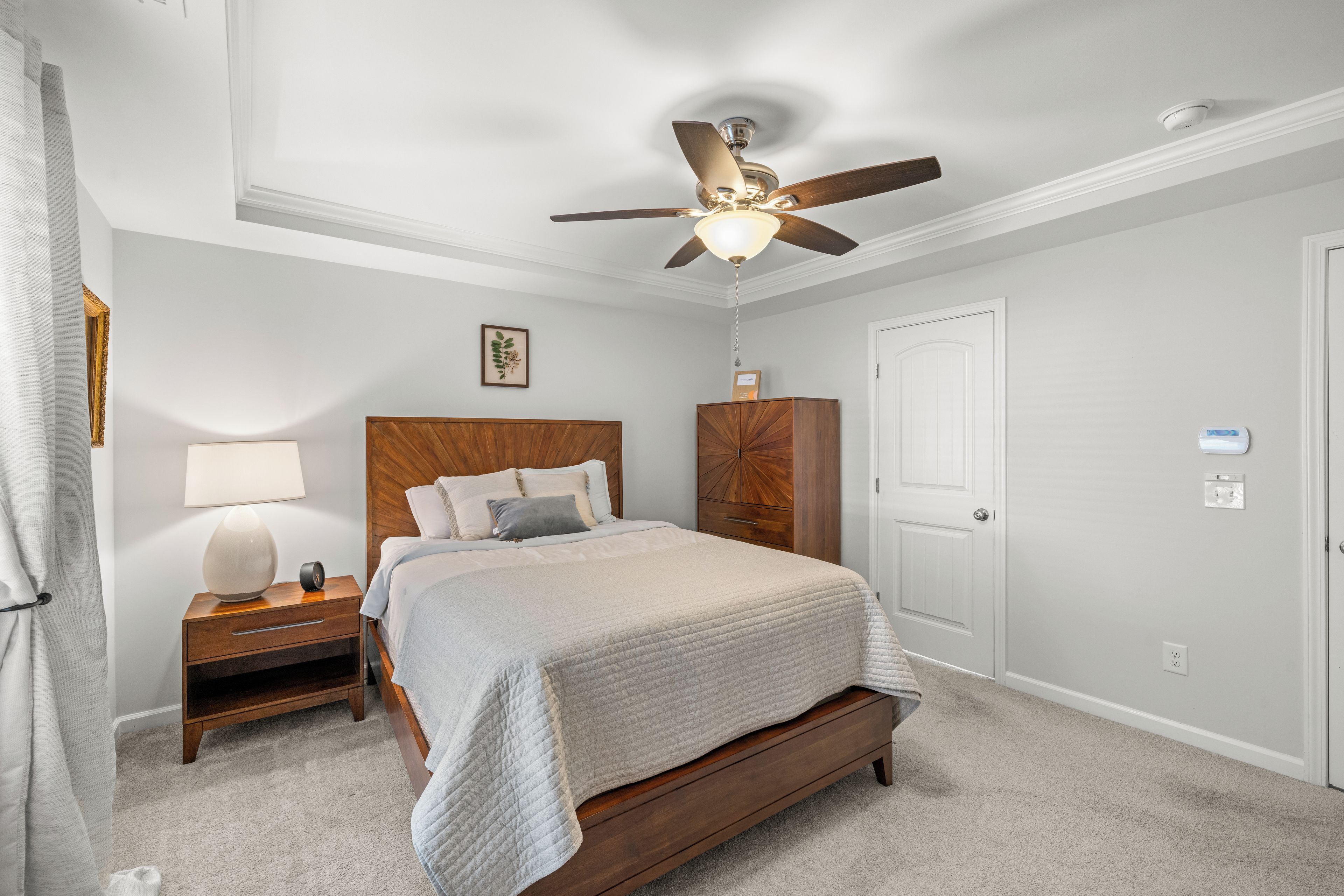 A bedroom with a bed, nightstand, lamp, ceiling fan, and a door.