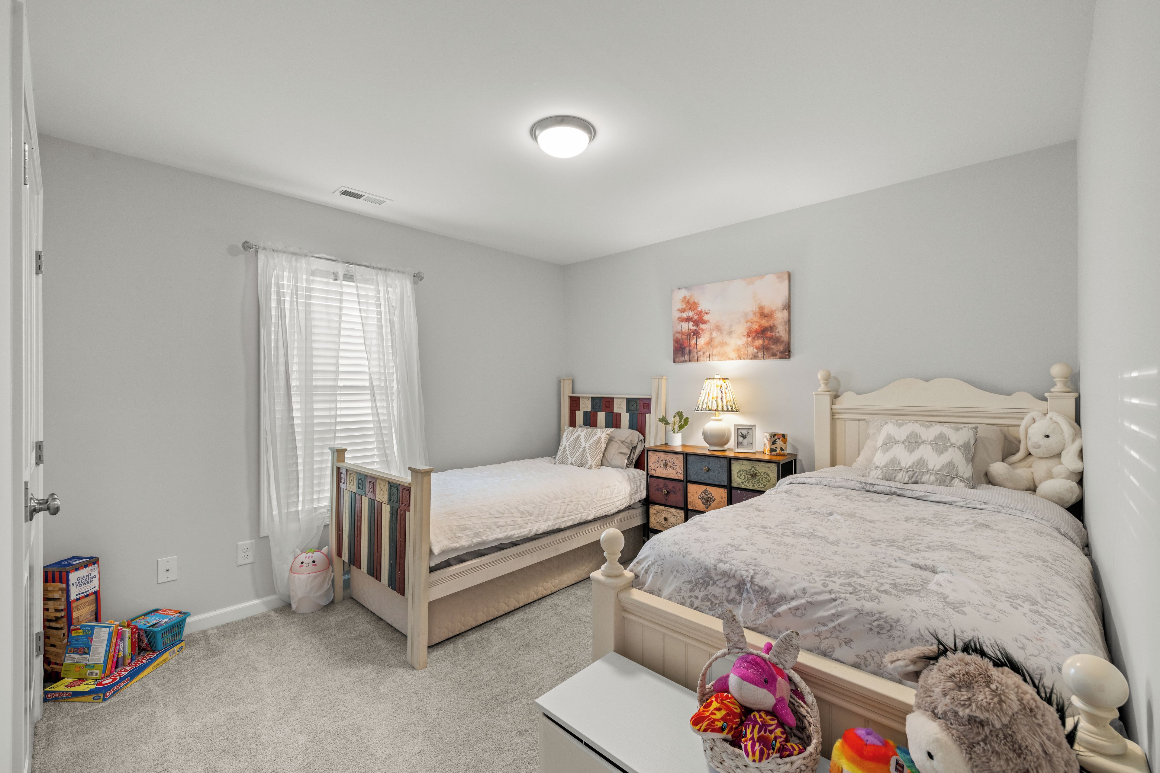 Une chambre avec deux lits simples, une table de chevet avec une lampe, une commode et un tableau accroché au mur.
