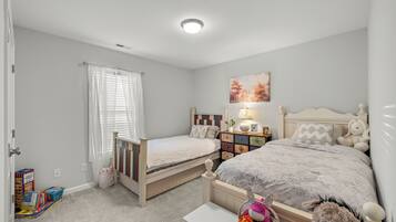 Une chambre avec deux lits simples, une table de chevet avec une lampe, une commode et un tableau accroché au mur.