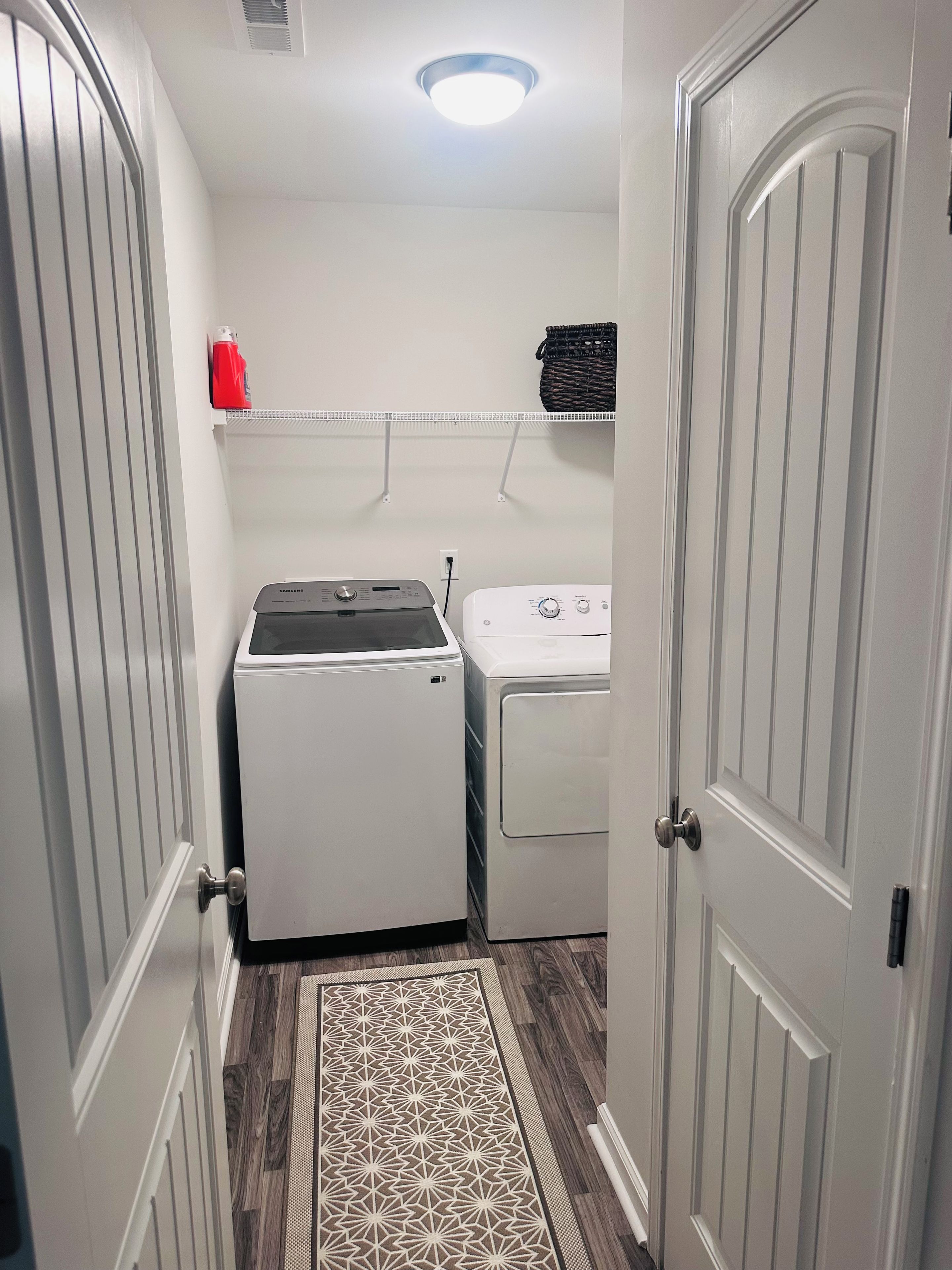 A laundry room with a washing machine, dryer, and a shelf with a red container.