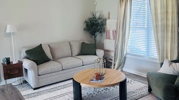 A living room with a ceiling fan, a sofa, a coffee table, a lamp, and a window with curtains.