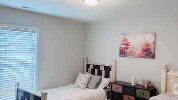 A bedroom with two beds, a window with blinds, a ceiling light, and a wall-mounted painting.