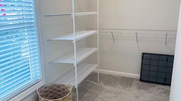 A room with a carpeted floor, a window with blinds, a metal shelving unit, and a woven basket.