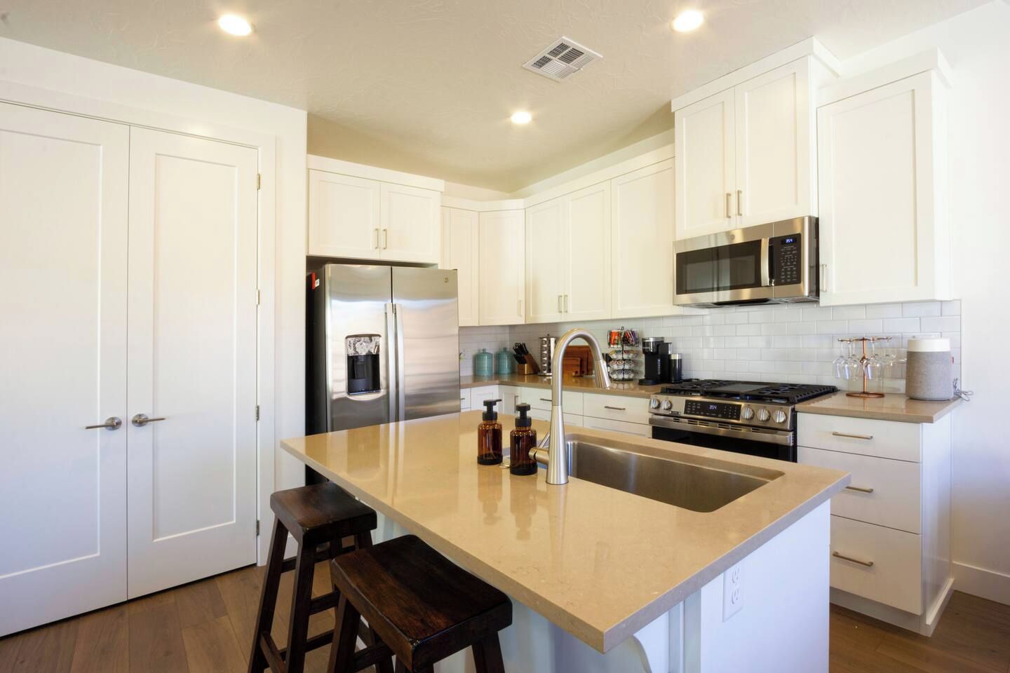 A modern kitchen with white cabinetry, stainless steel appliances, and a central island with stools.
