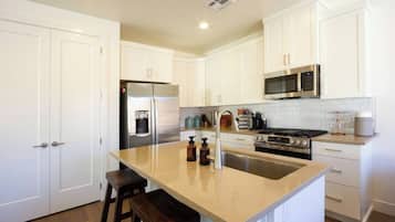 A modern kitchen with white cabinetry, stainless steel appliances, and a central island with stools.