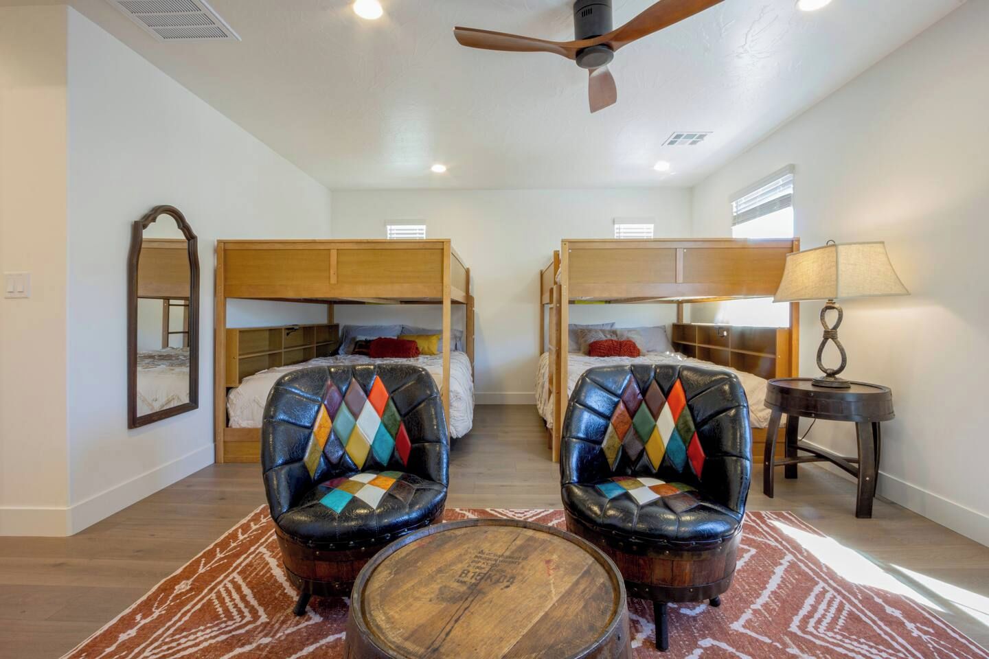 A room with two bunk beds, a mirror, a lamp, and two leather armchairs.