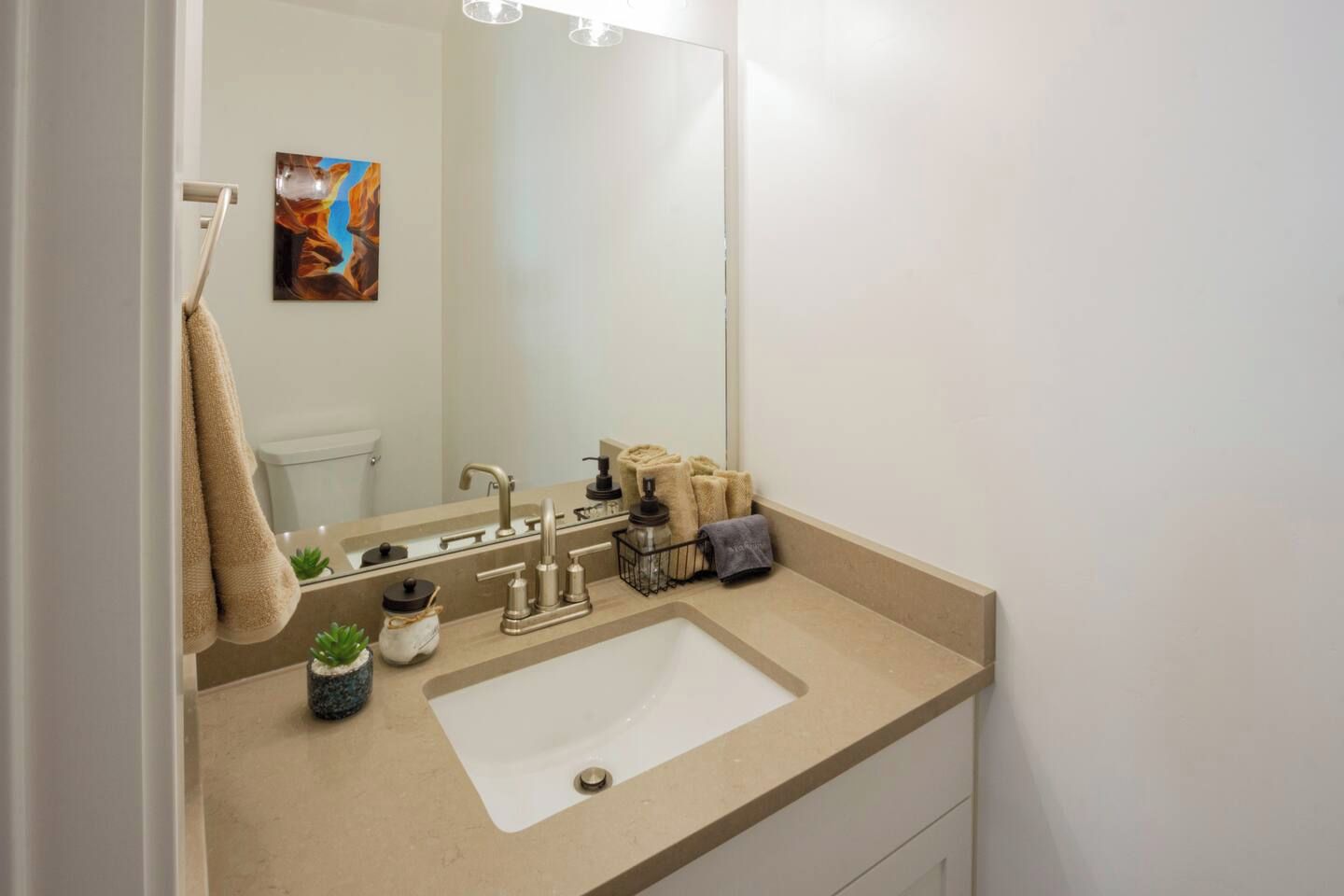 A bathroom with a beige countertop, a white sink, a mirror, and a towel rack.