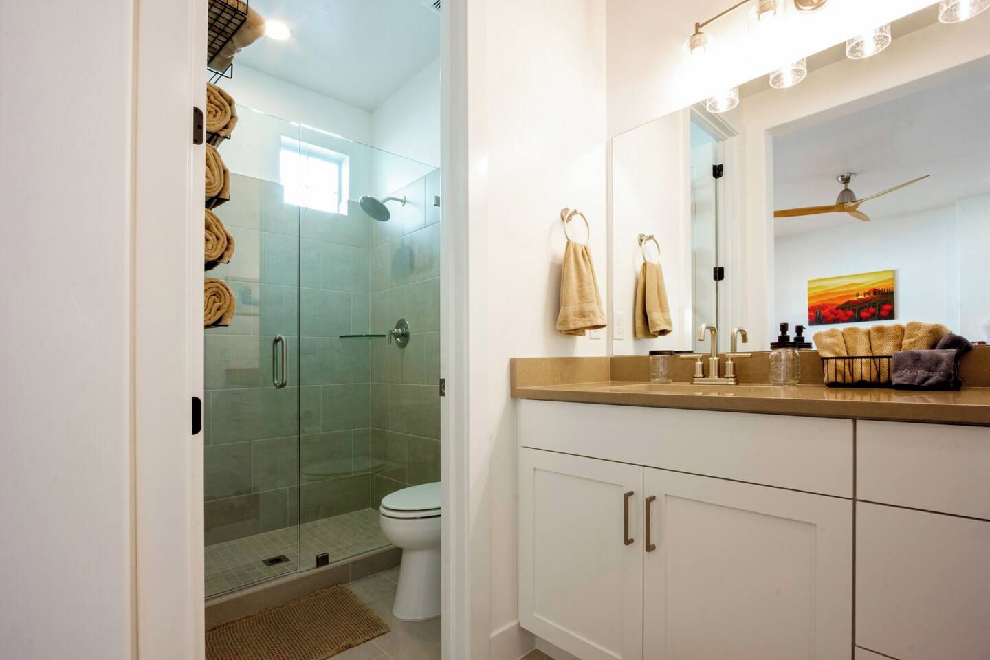 A bathroom with a glass-enclosed shower, a toilet, a vanity with a mirror, and towels.