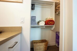 Un placard avec des étagères où sont rangés des vêtements pliés et un panier.