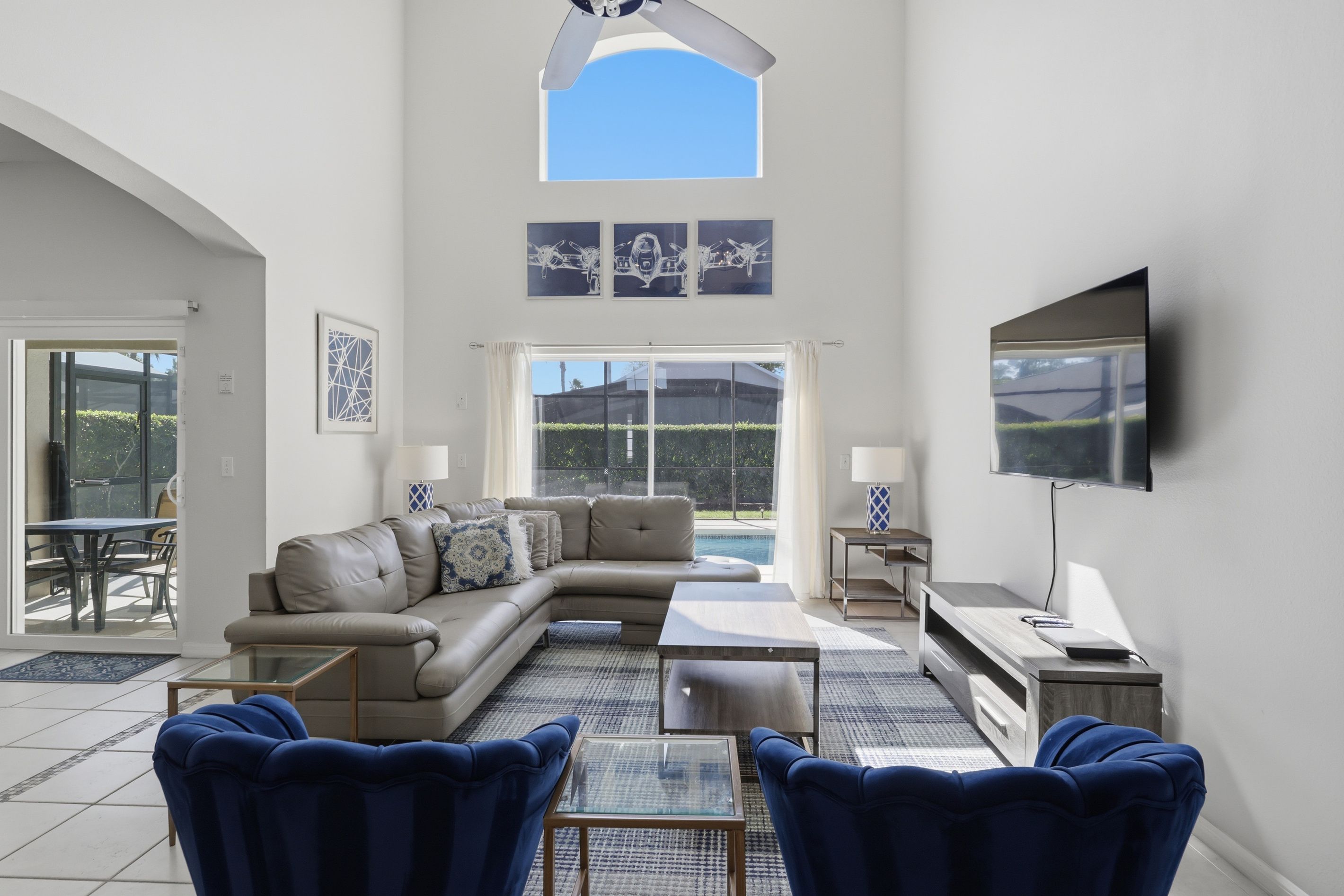 A spacious living room with a large sectional sofa, a glass coffee table, and a flat-screen TV mounted on the wall.