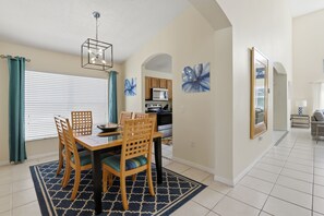 A dining area with a wooden table and chairs, a chandelier, and a kitchen in the background. - Amazing Retreat at Lake Berkley (Kissimmee)