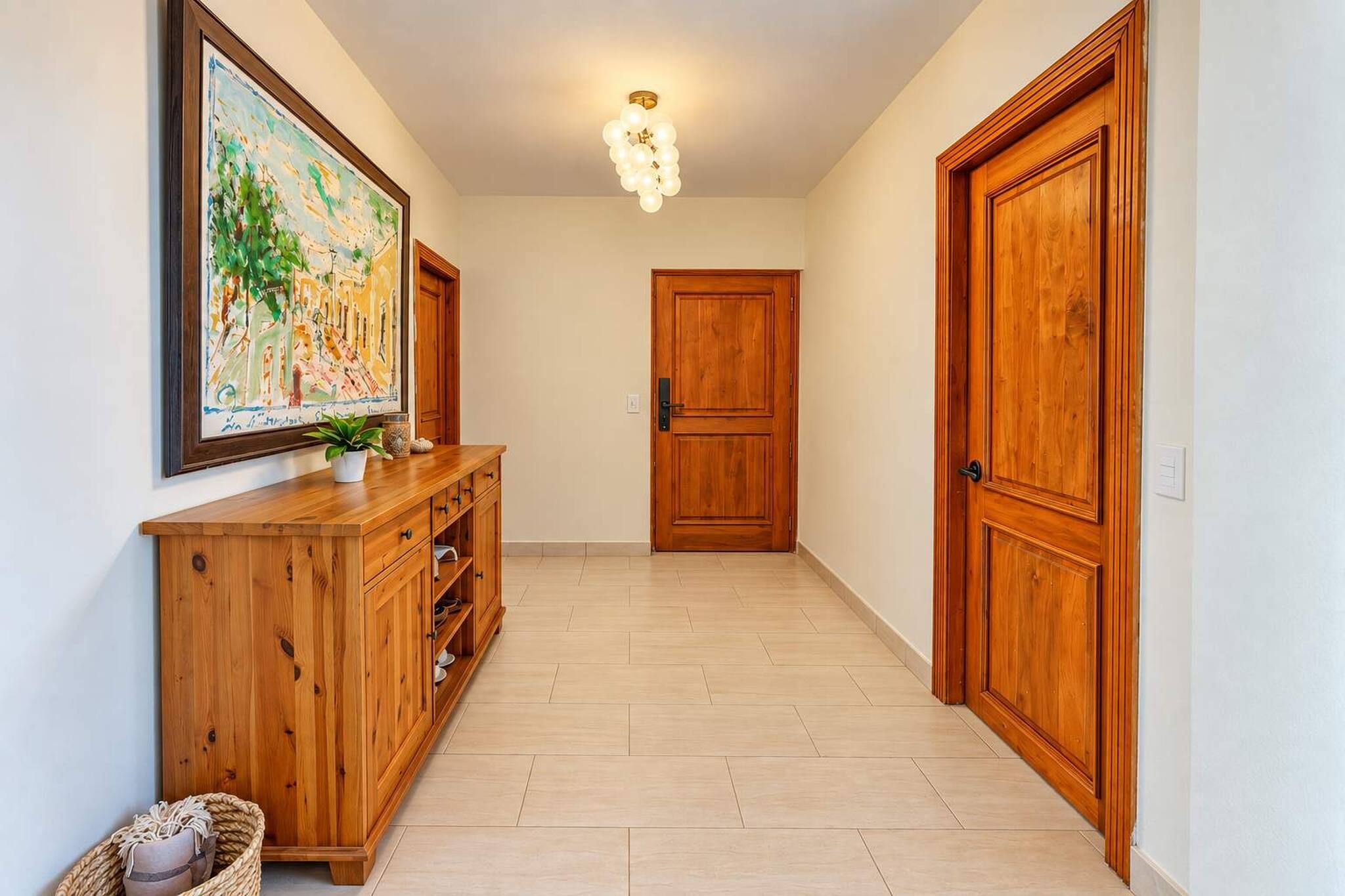 A hallway with wooden doors, a wooden cabinet with drawers, a hanging painting, and a ceiling light fixture.