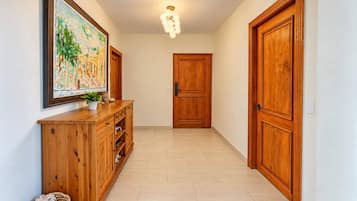 A hallway with wooden doors, a wooden cabinet with drawers, a hanging painting, and a ceiling light fixture.