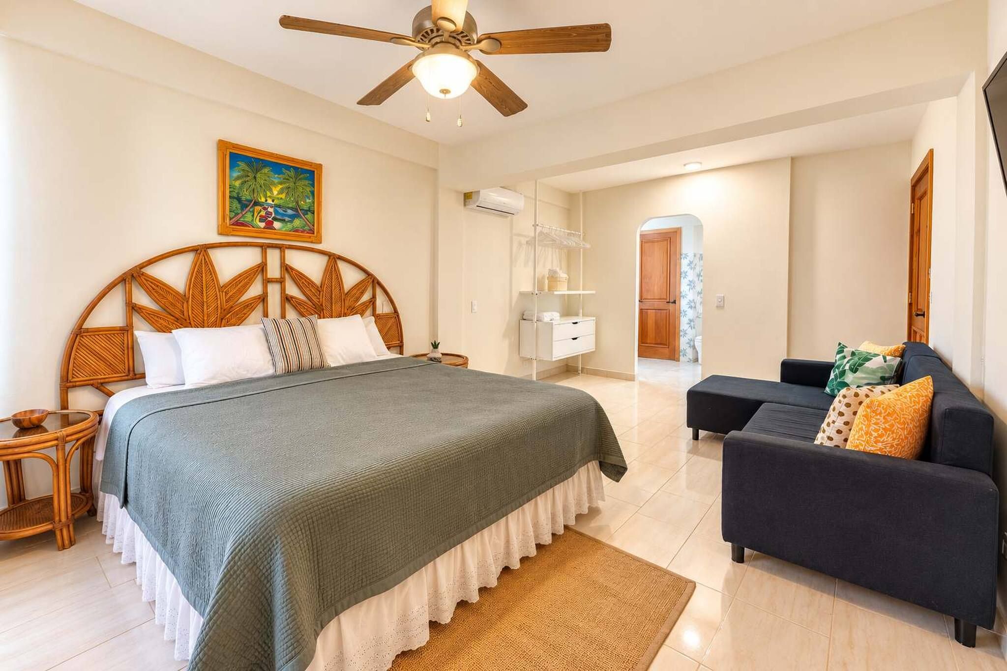 Un dormitorio con cama, ventilador de techo, un cuadro, armario y sofá.
